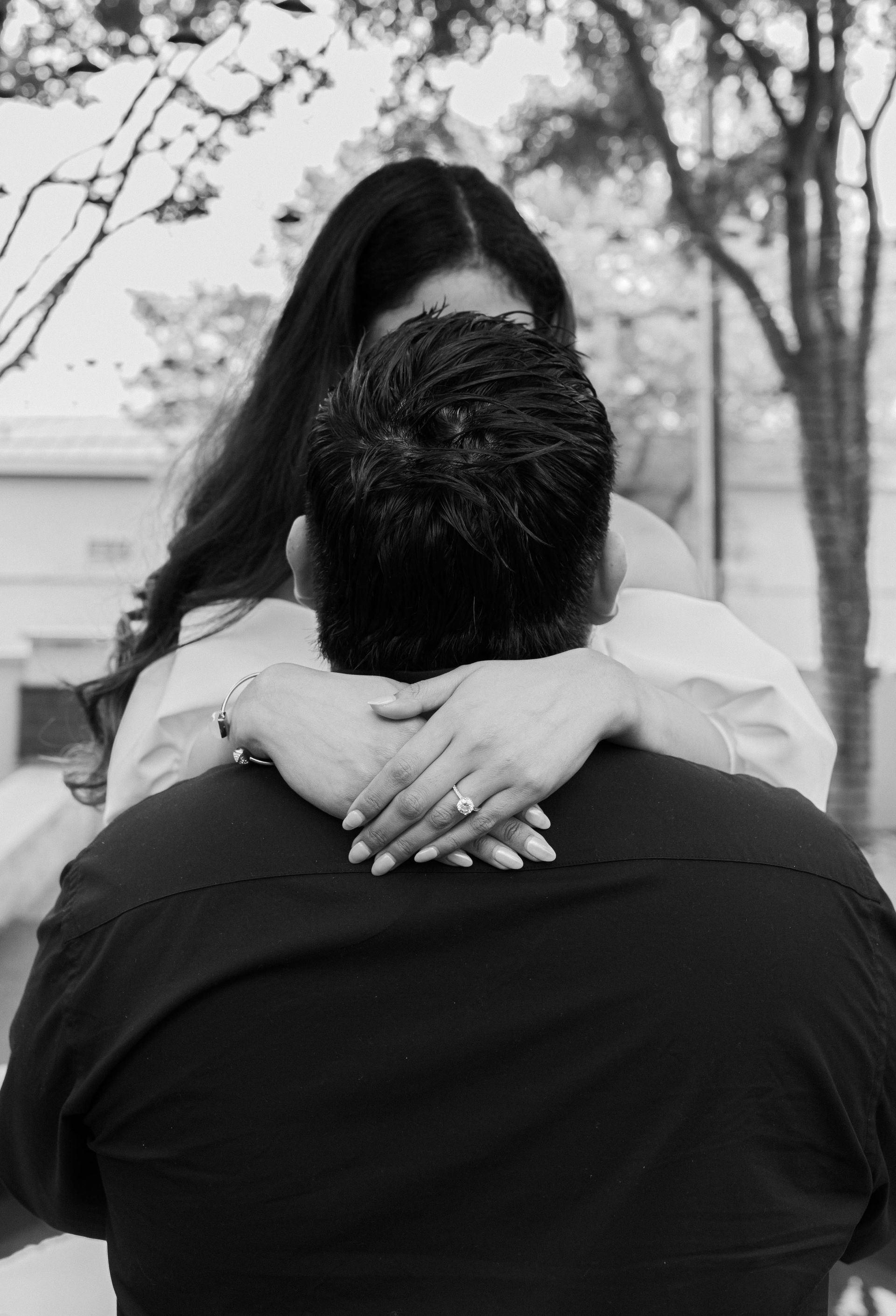 A black and white photo of a woman hugging a man.