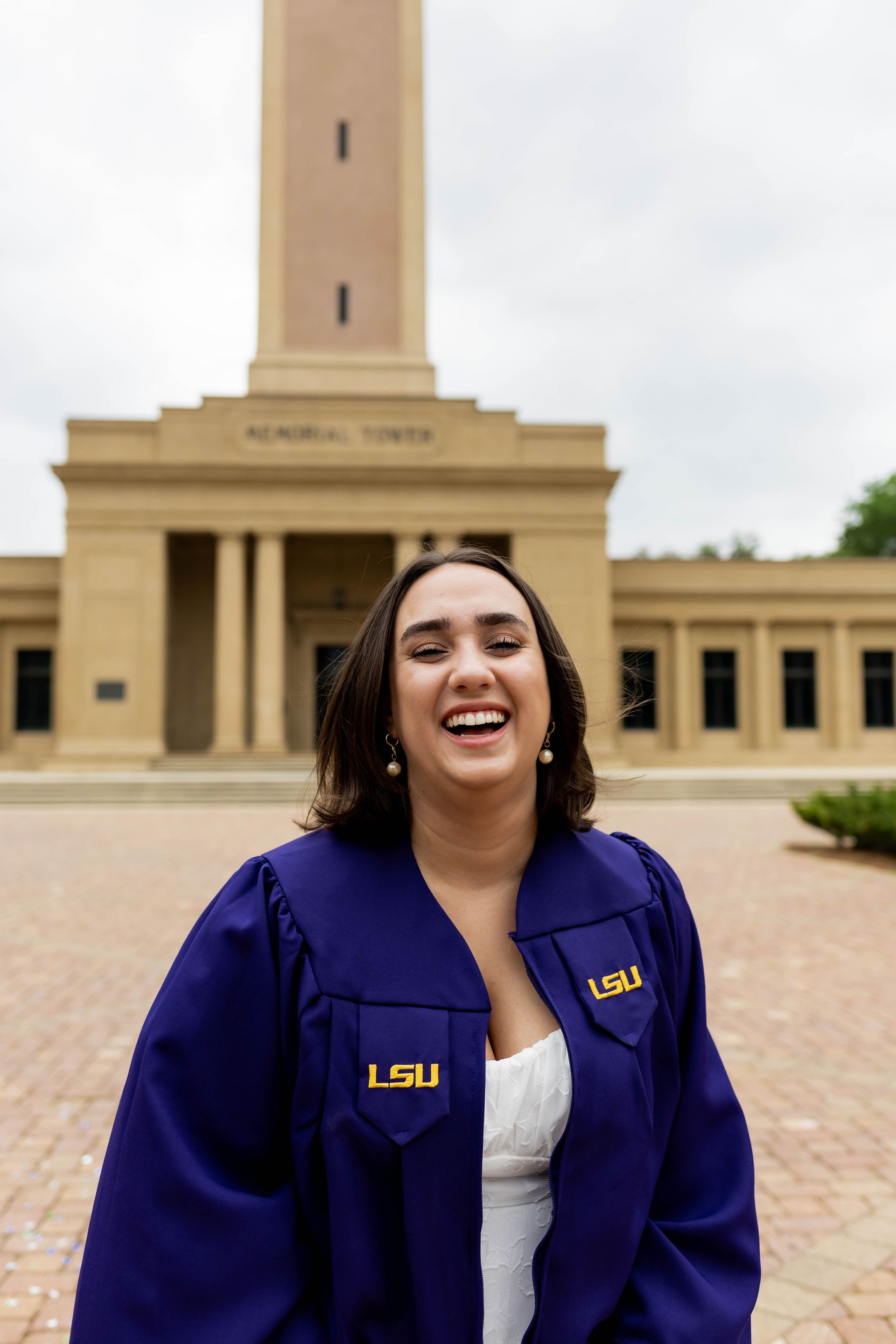 A woman in a purple graduation cap and gown is standing in front of a building.