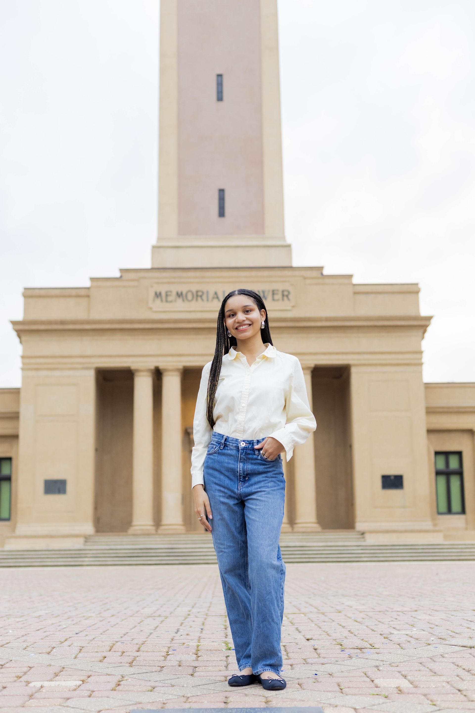 A woman in a white shirt and blue jeans is standing in front of a building.