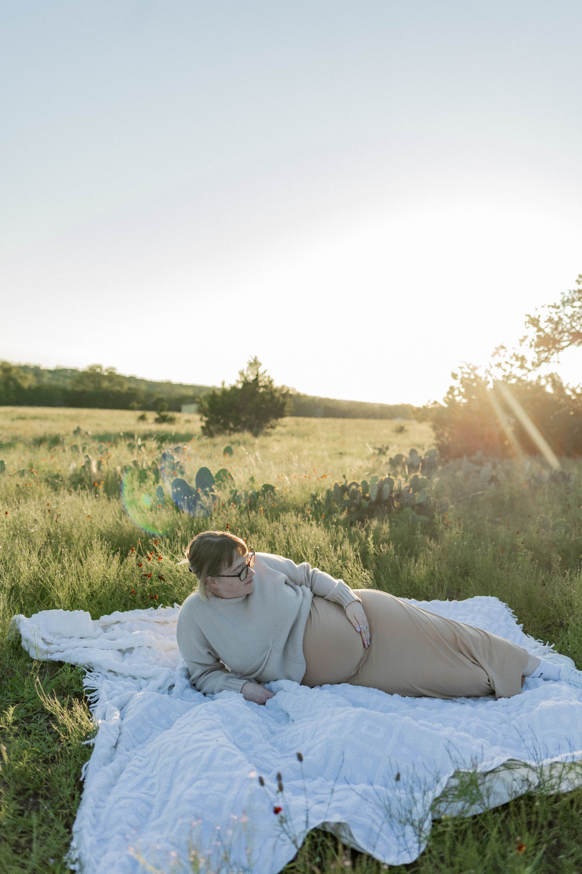 A pregnant woman is laying on a blanket in a field.
