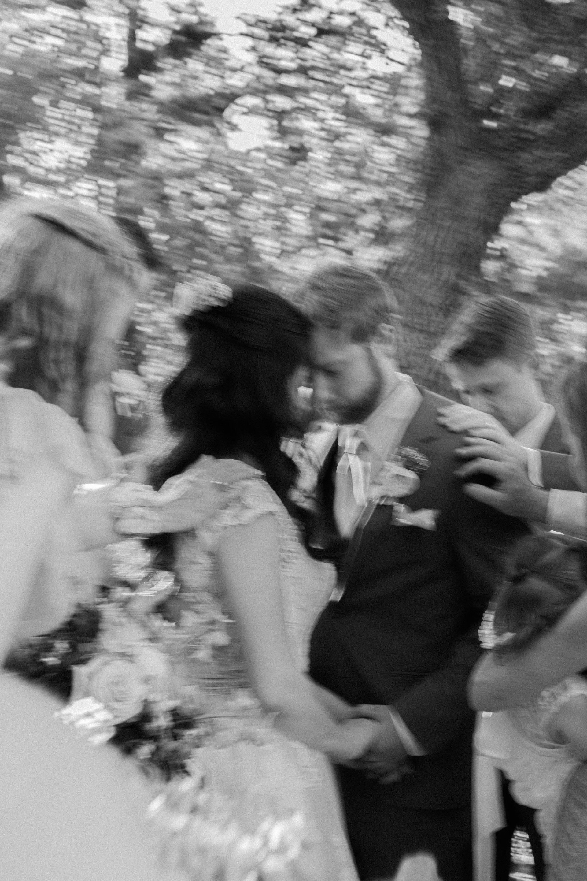 A black and white photo of a bride and groom holding hands at their wedding ceremony.
