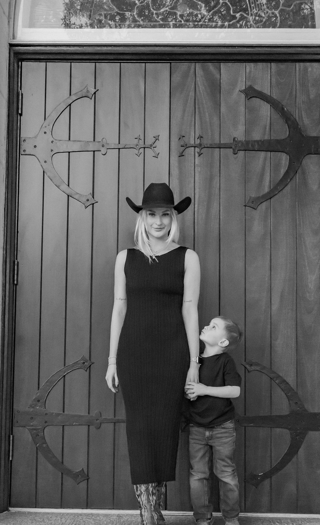 A woman and a boy are standing in front of a wooden door.