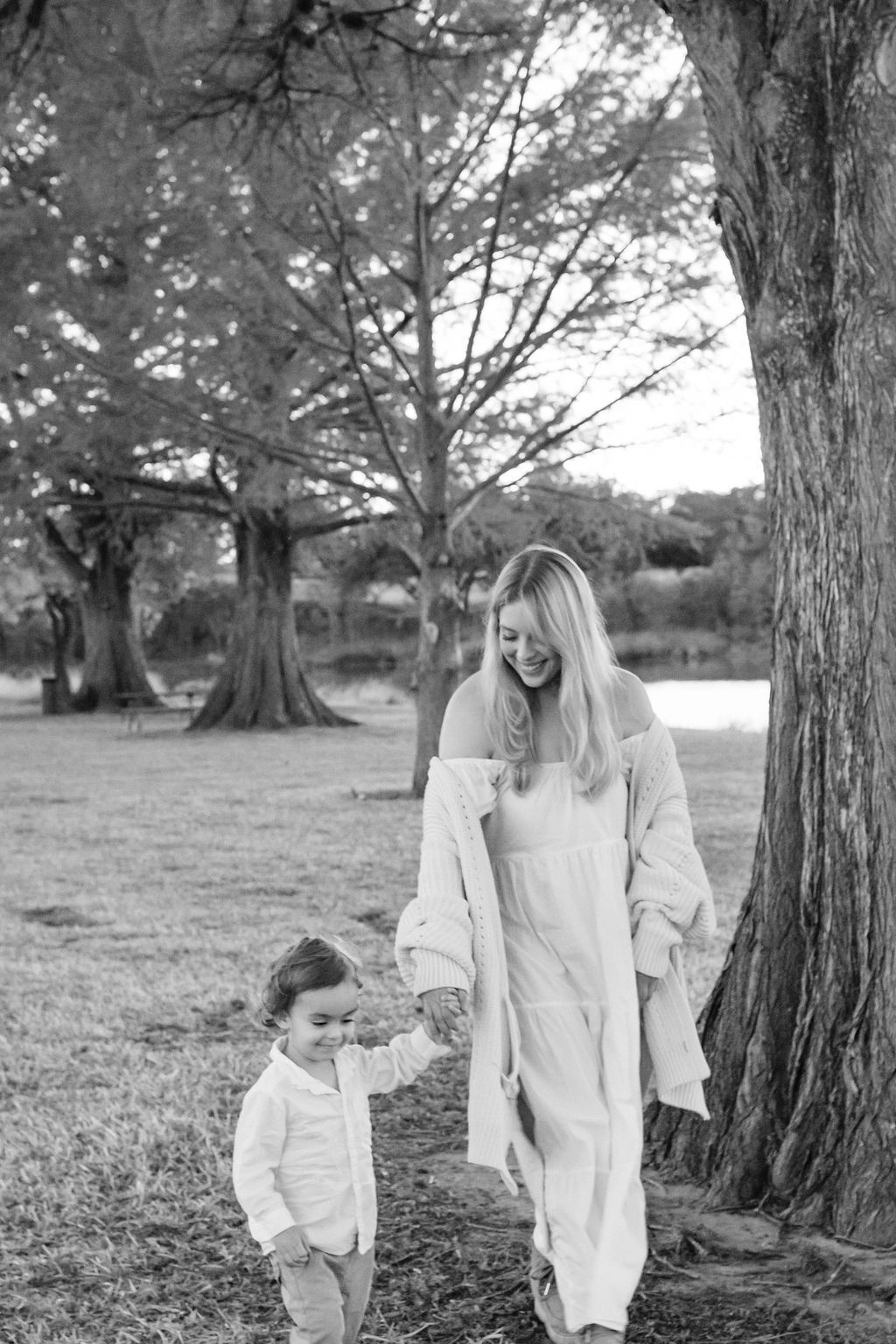 A woman and a child are walking in a park holding hands.
