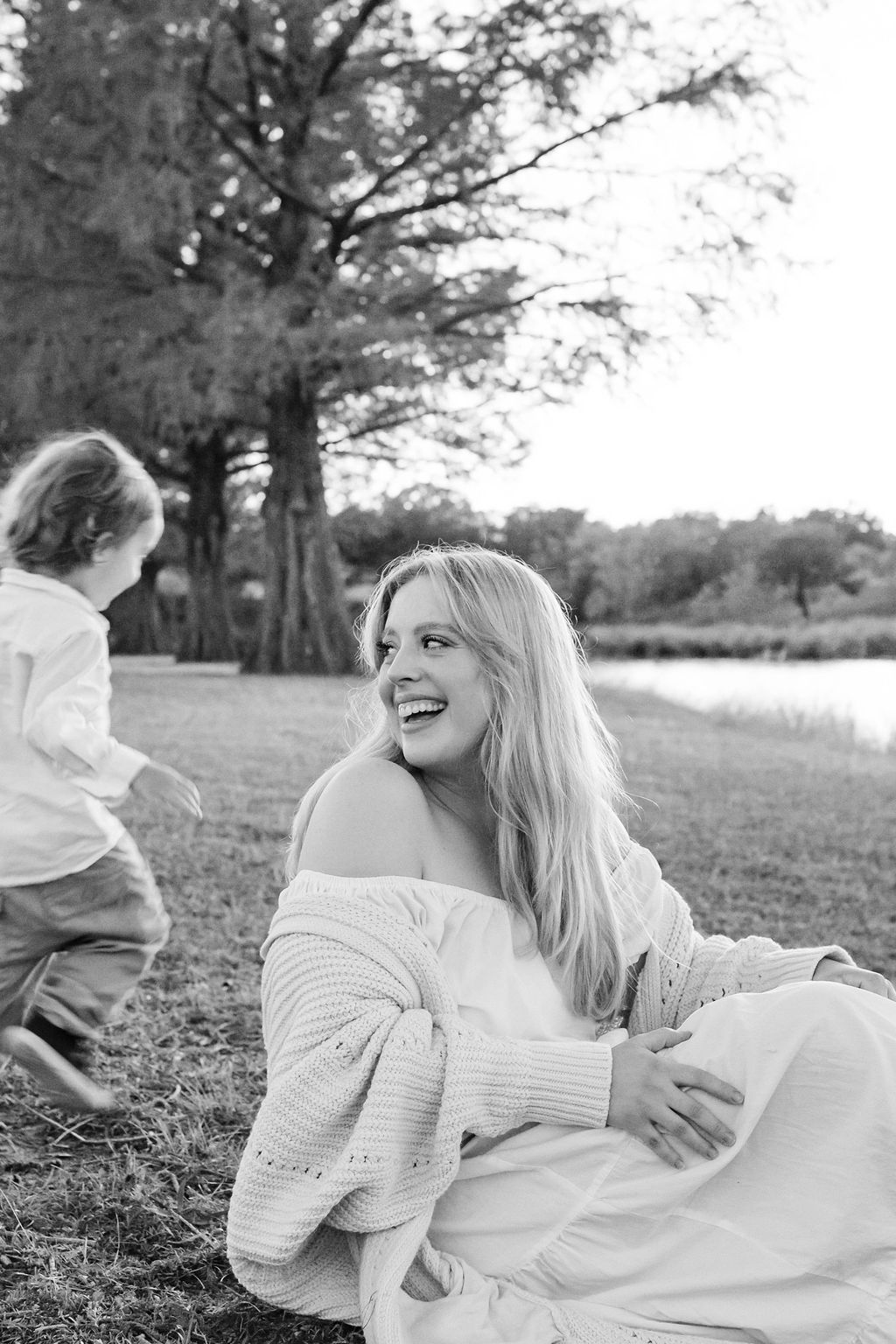 A black and white photo of a pregnant woman sitting in the grass with a child.