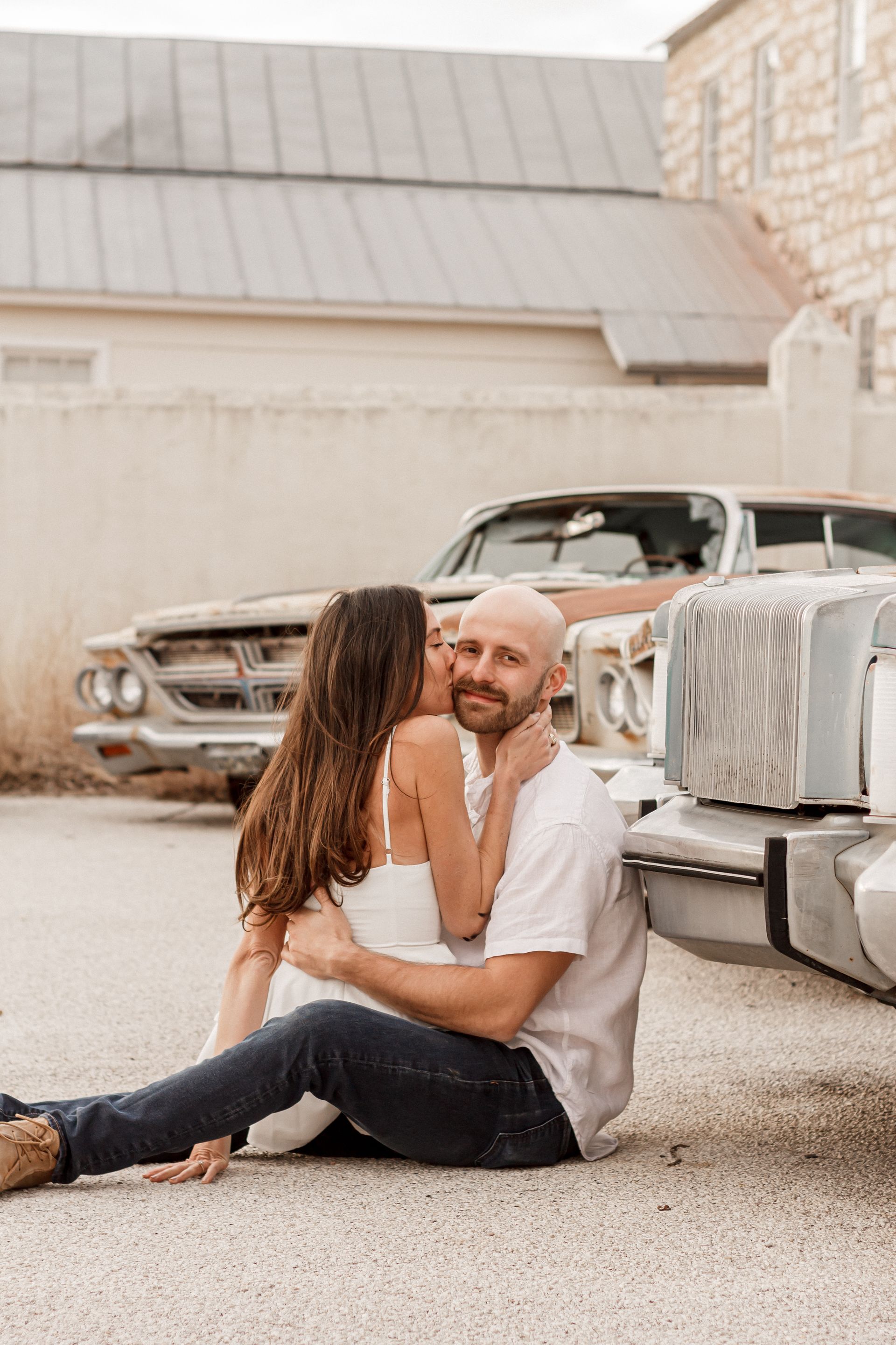 A man and a woman are sitting on the ground next to a car.