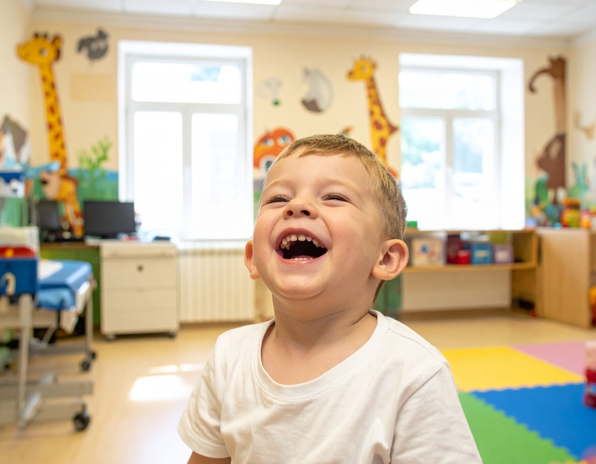 Child laughing in a bright classroom with colorful mats and toys in the background