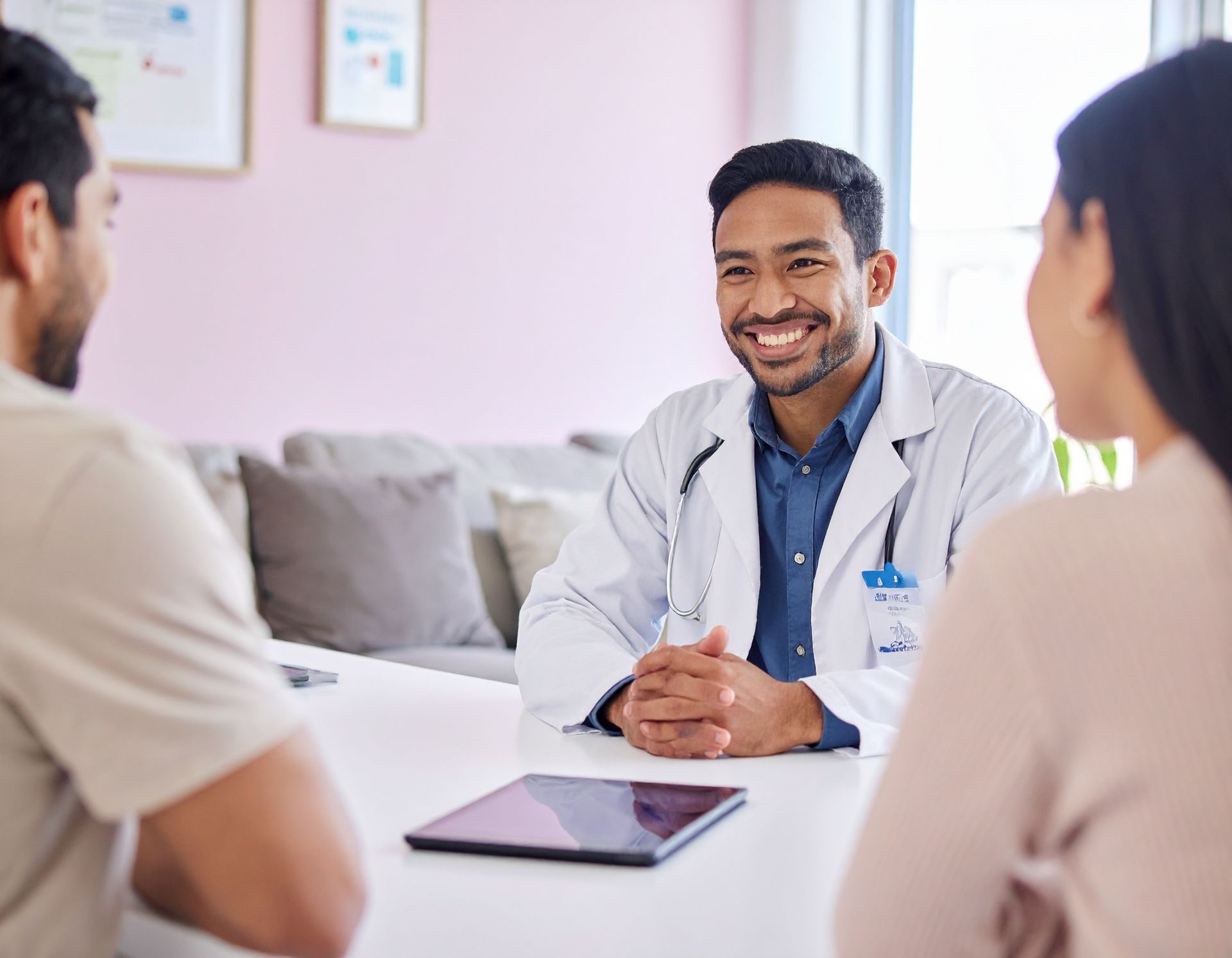 Doctor smiling during a consultation with two seated patients in a bright clinic room