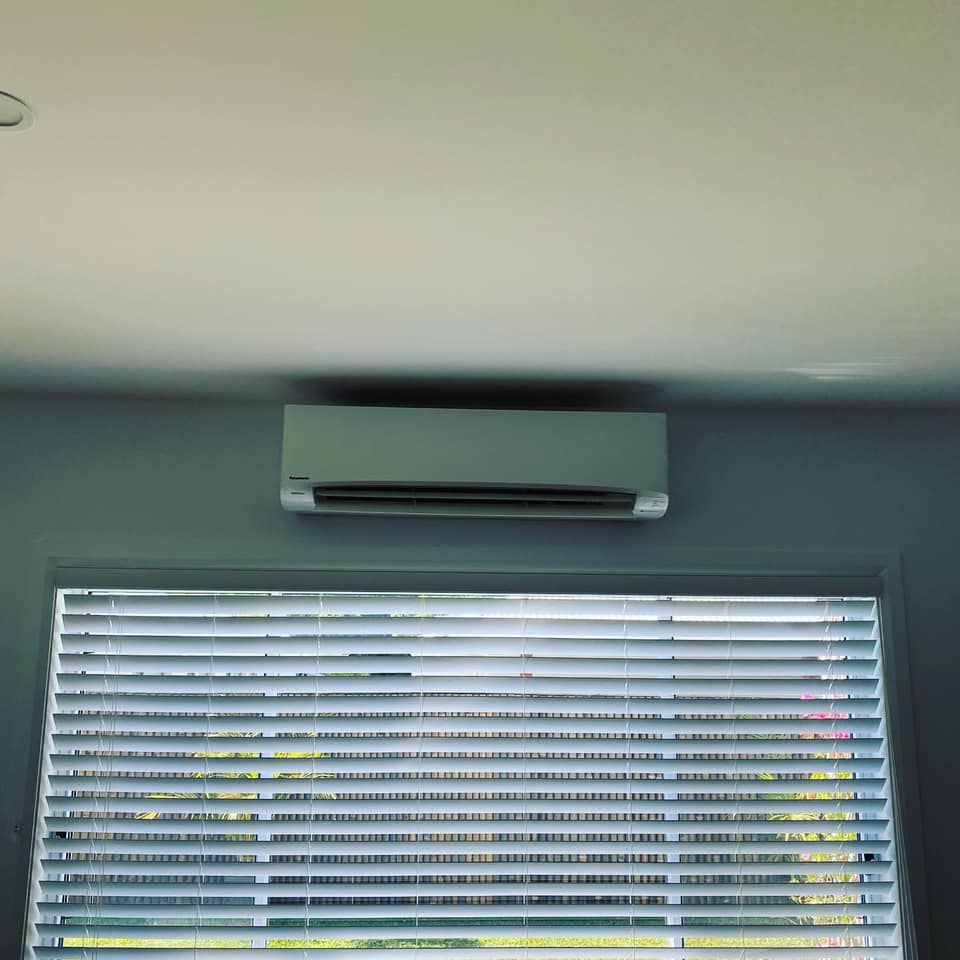Air Conditioner Mounted Above a Window With Blinds; White Wall and Ceiling — Airset Air Conditioning in Nambucca, NSW