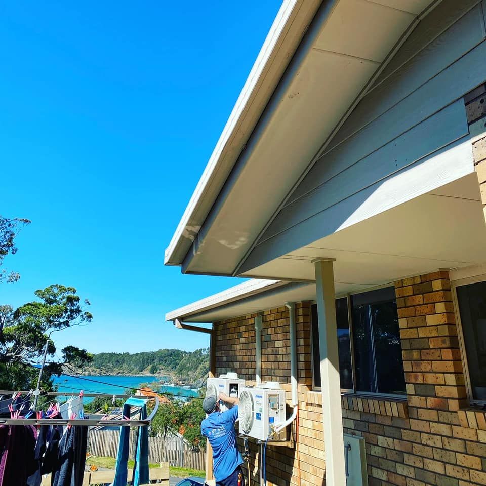 Person outdoors painting a brick house wall beside a lake under a bright blue sky — Airset Air Conditioning in Macksville, NSW