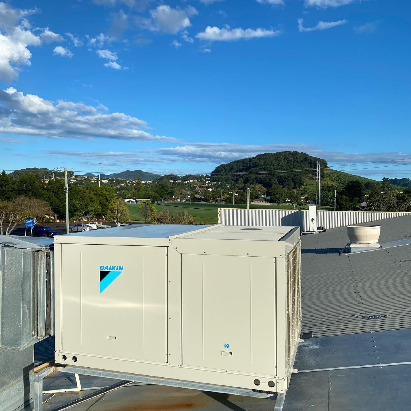 Beige rooftop HVAC unit on a flat roof with blue sky and trees in the background — Airset Air Conditioning in Macksville, NSW