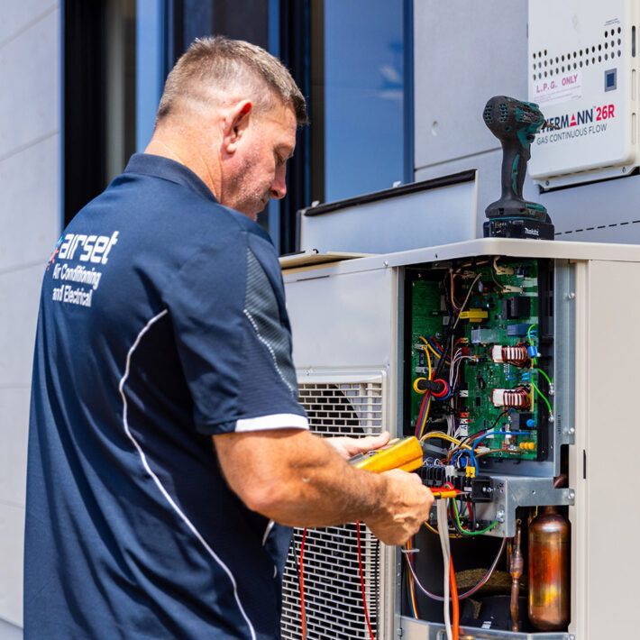 Man Fixing an Air Conditioner on a Wall, Outdoor Setting — Airset Air Conditioning in Urunga, NSW