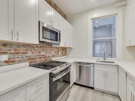A kitchen with white cabinets , stainless steel appliances , and a brick wall.