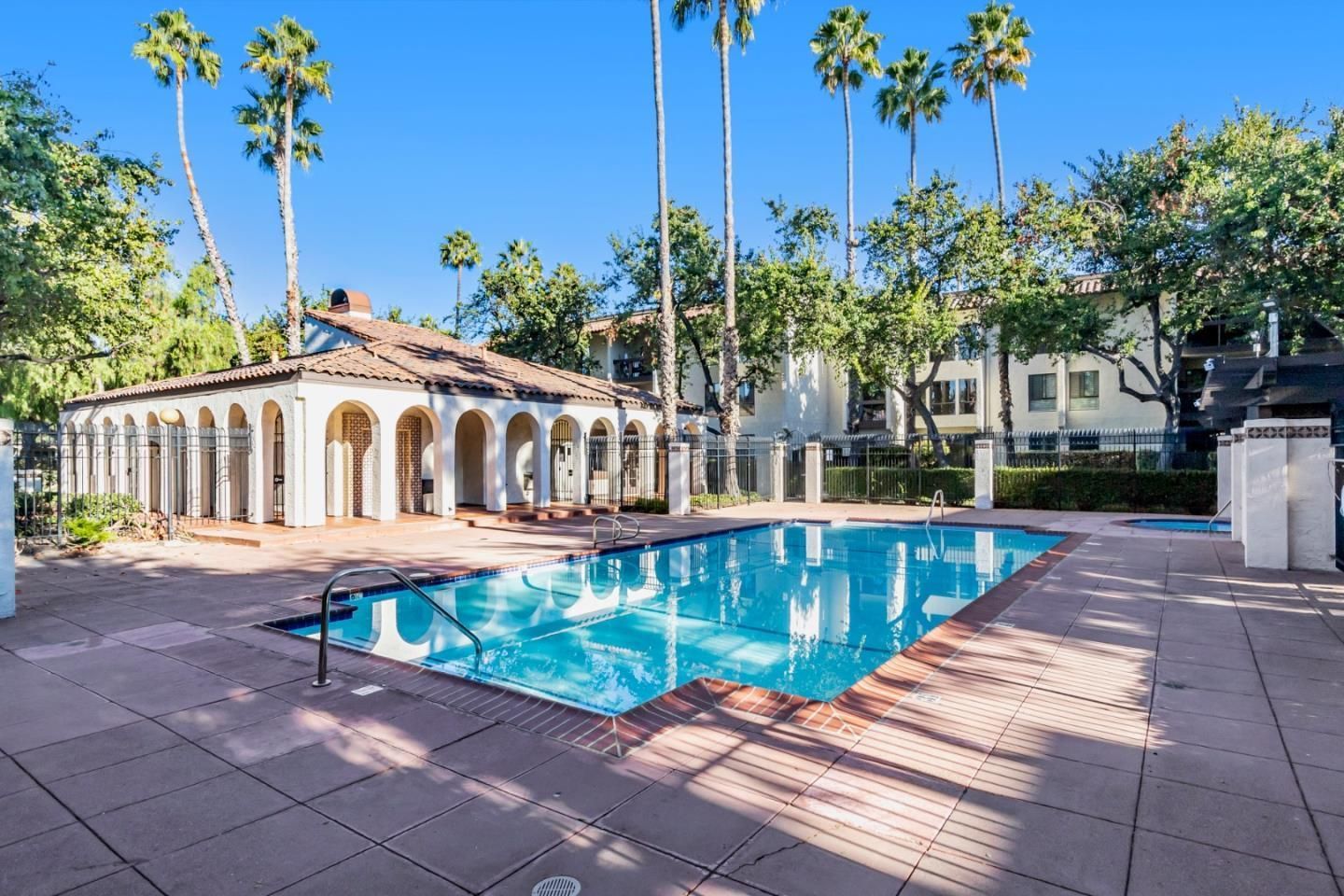 A large swimming pool is surrounded by palm trees and a building.