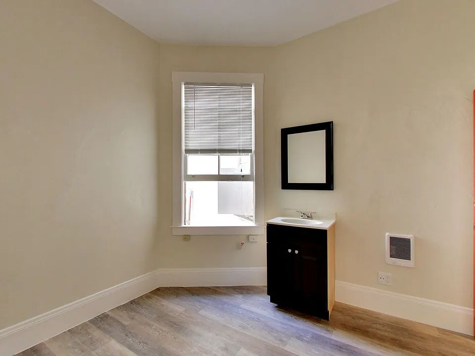 An empty room with a sink , mirror and window.