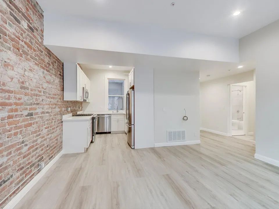 An empty room with a brick wall and a kitchen.