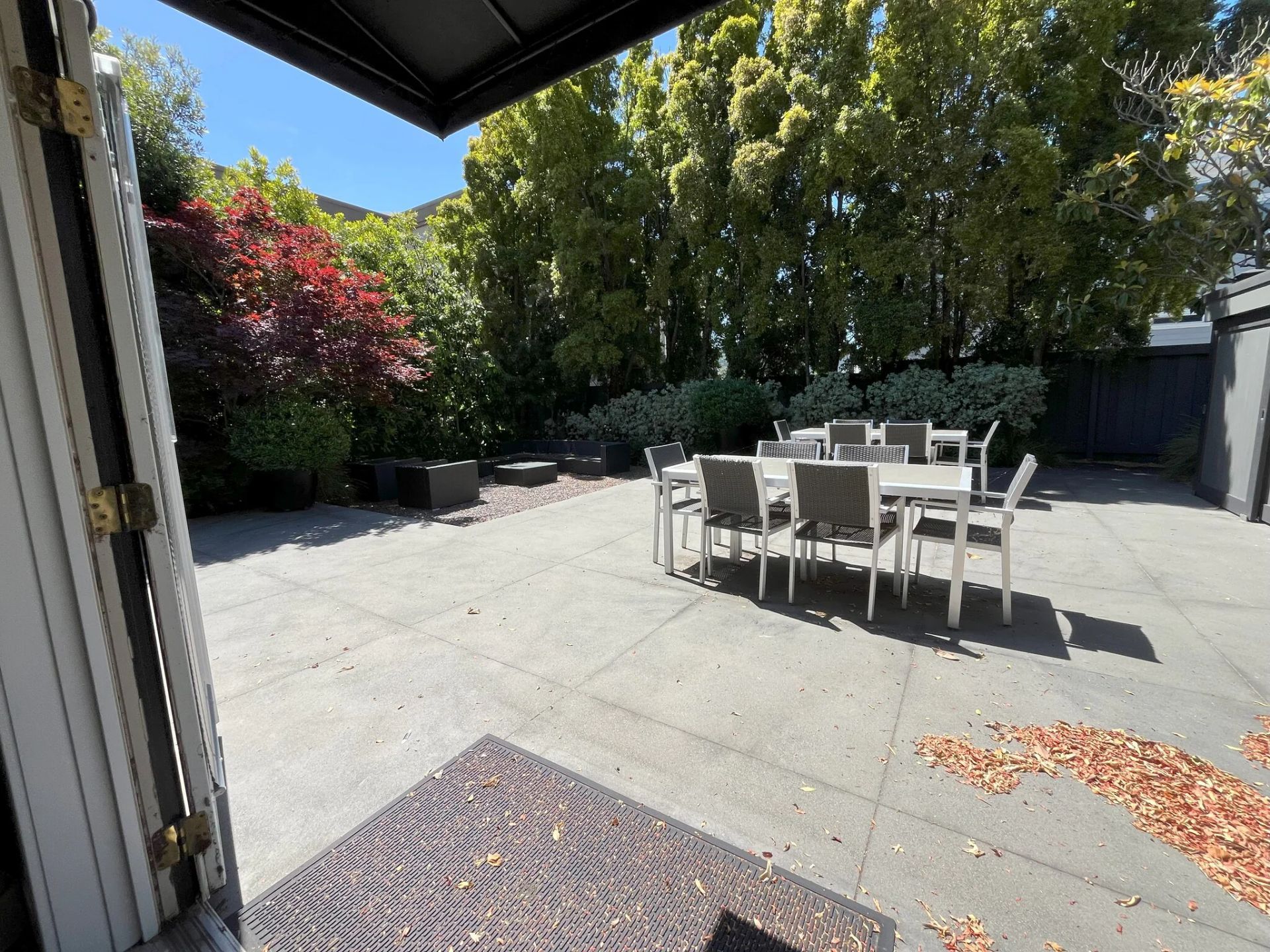 Patio with table and chairs, surrounded by greenery and trees.