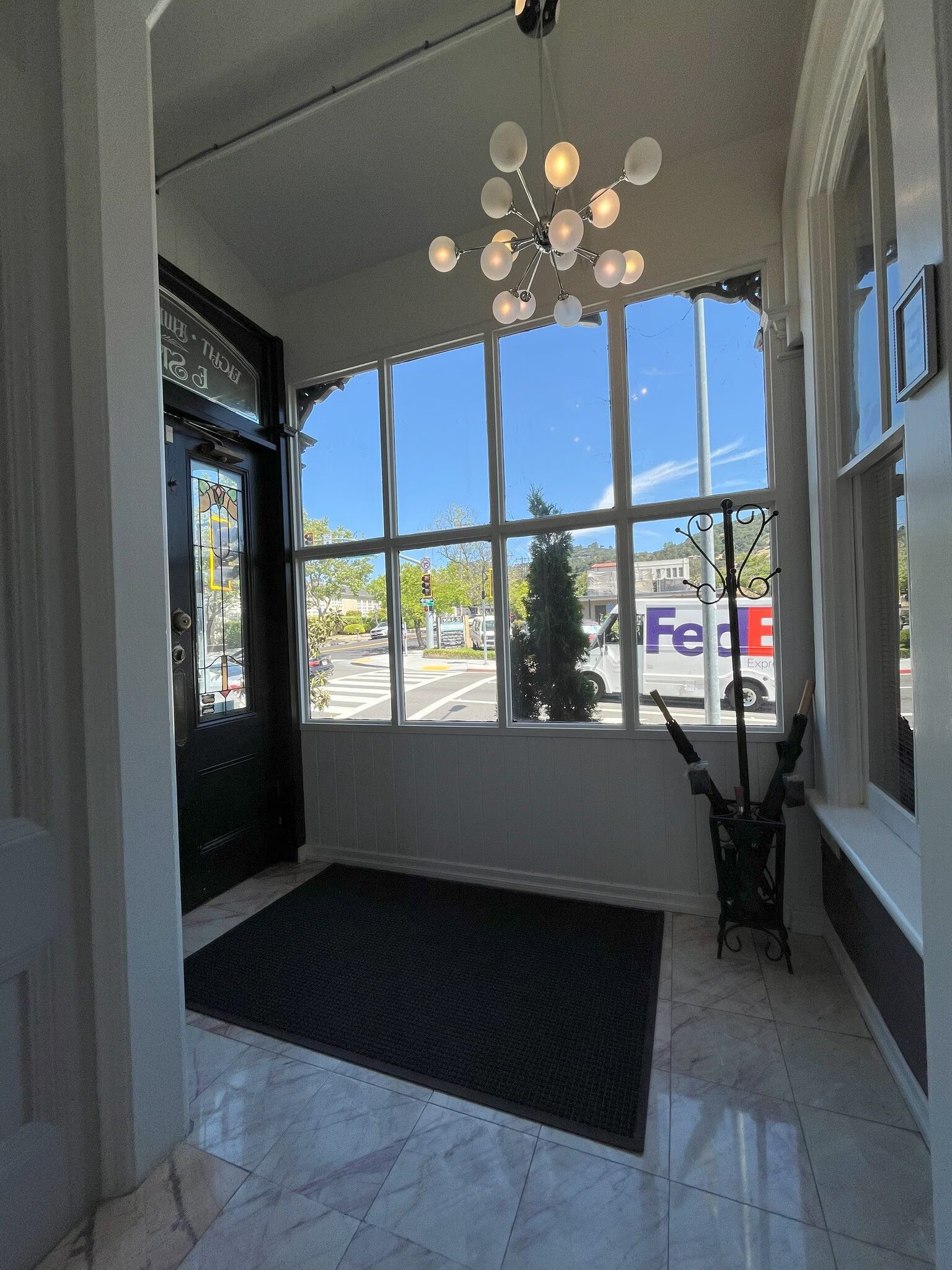 Entryway with large windows overlooking a street. Black door, dark rug, and decorative light fixture.