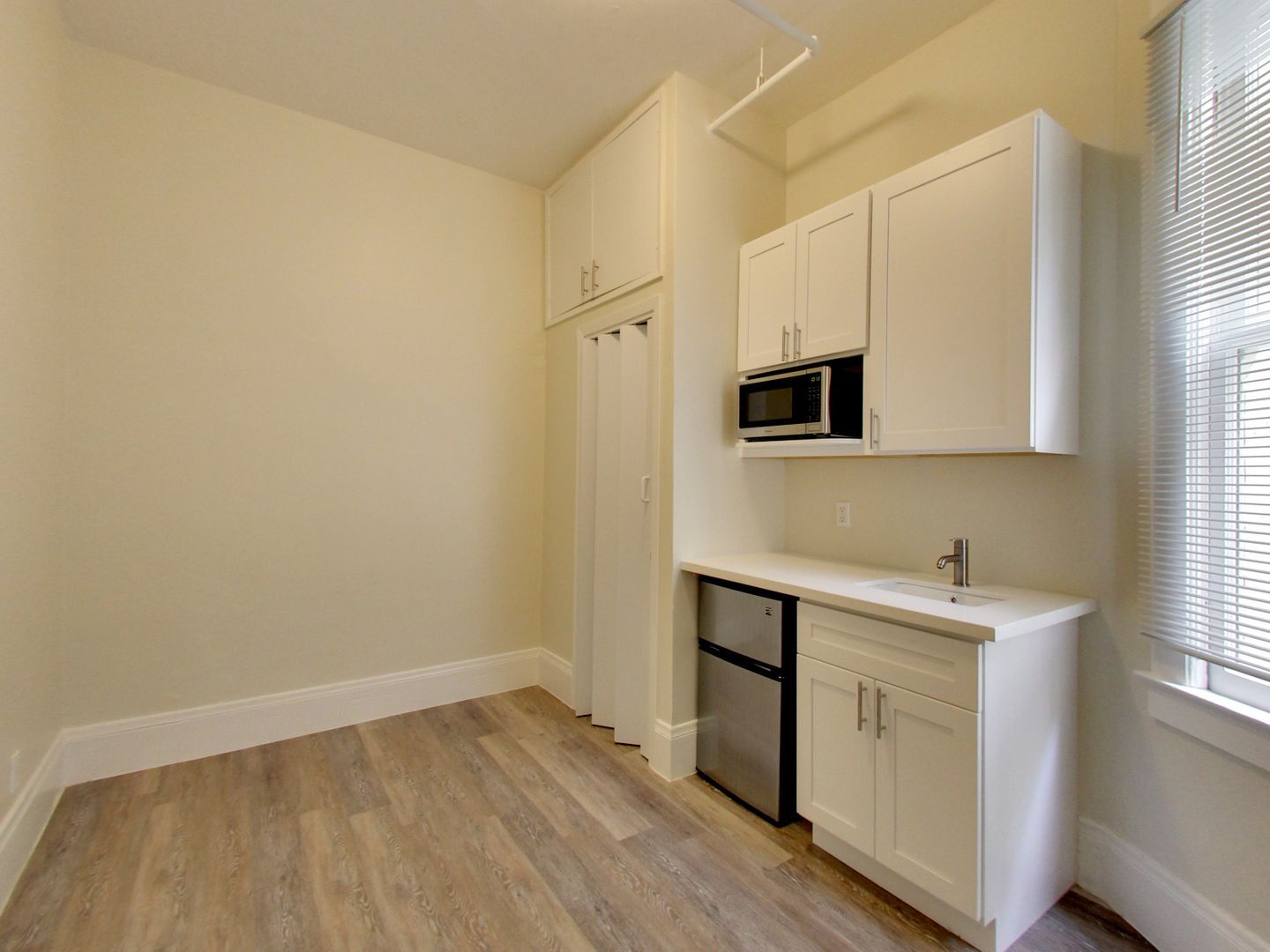 A kitchen with white cabinets , a sink , a microwave , and a refrigerator.
