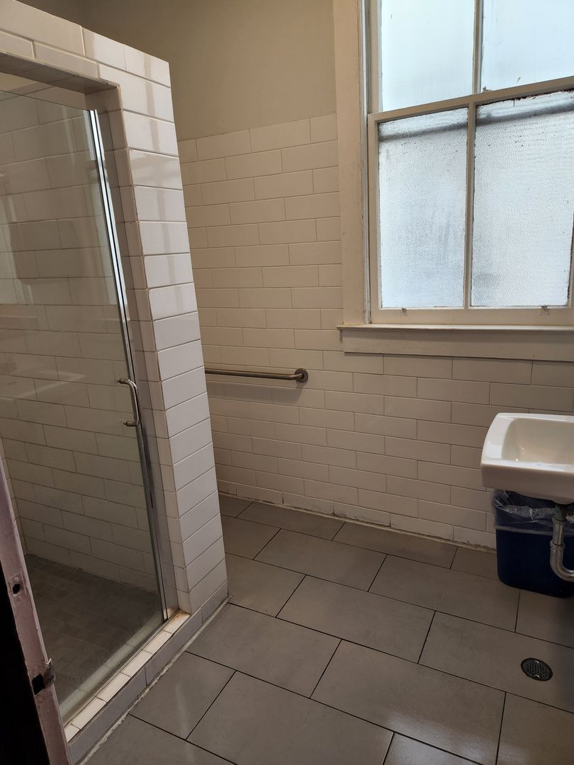 A bathroom with a sink , shower , and window.
