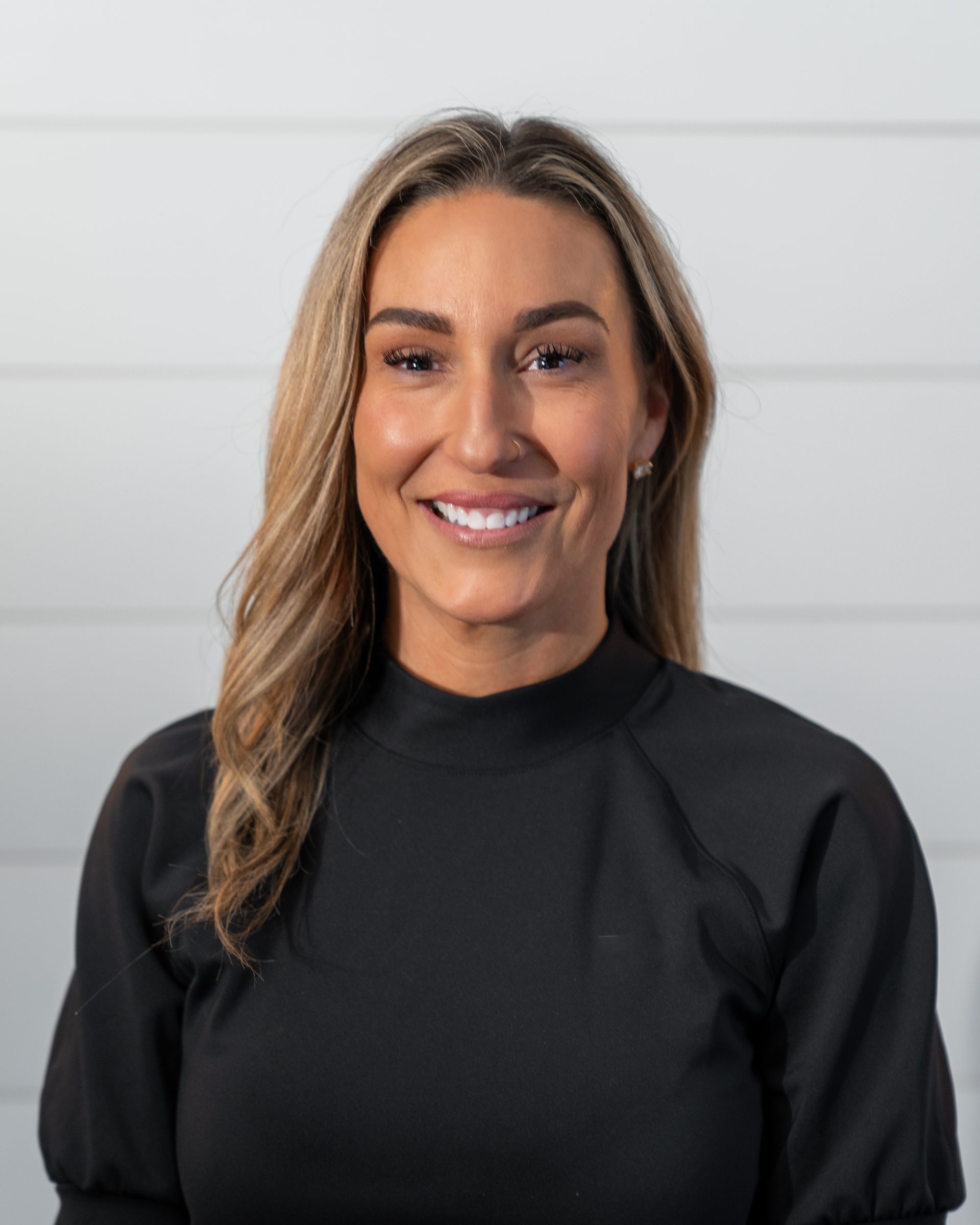 A woman wearing a black shirt and a necklace is smiling for the camera.