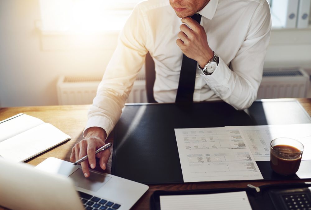 A Man is Sitting at a Desk With a Laptop and Papers — Townsville Accounting In Hyde Park, QLD