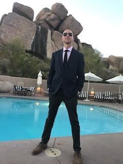A man in a suit and tie is standing next to a swimming pool.