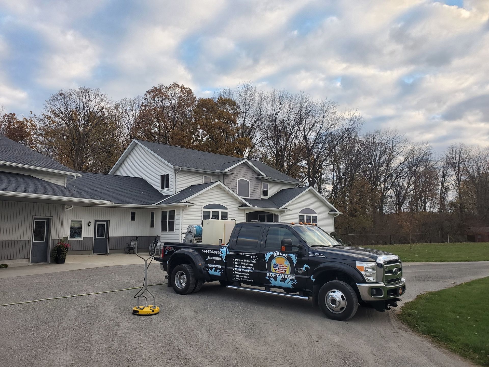 A black work truck with logos parked on a gravel driveway in front of a white building with a grey roof.