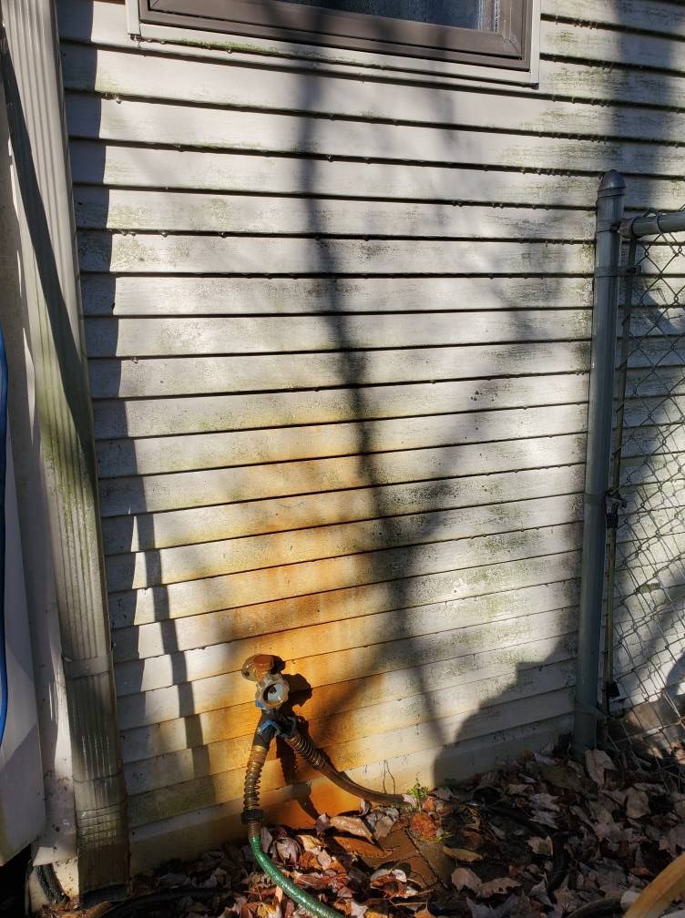Outdoor water spigot attached to light gray siding, showing significant orange rust staining running down the wall.