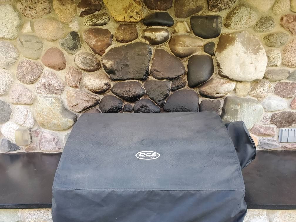 A black protective cover with a DCS logo rests on a dark surface in front of a natural stone wall.