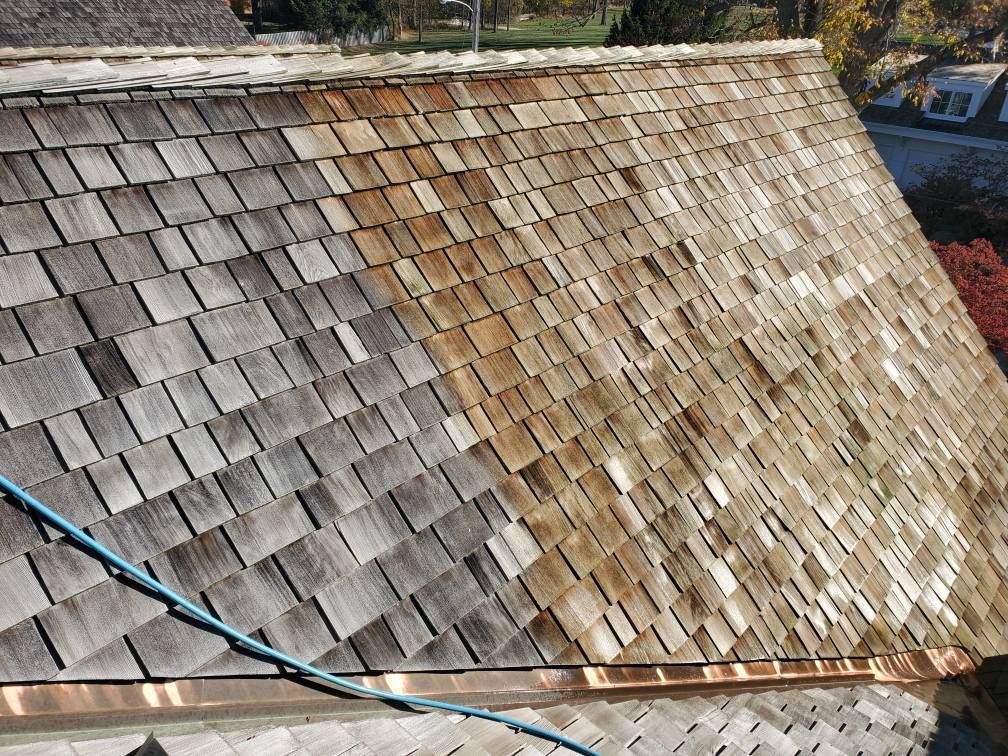 A cedar shake roof showing a contrast between weathered grey shingles on the left and cleaned, natural wood on the right.
