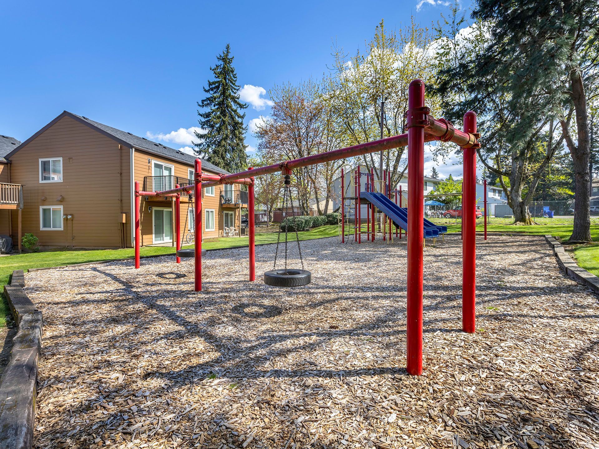 Photo of a community playground featuring a swing, tire swing, slide and more