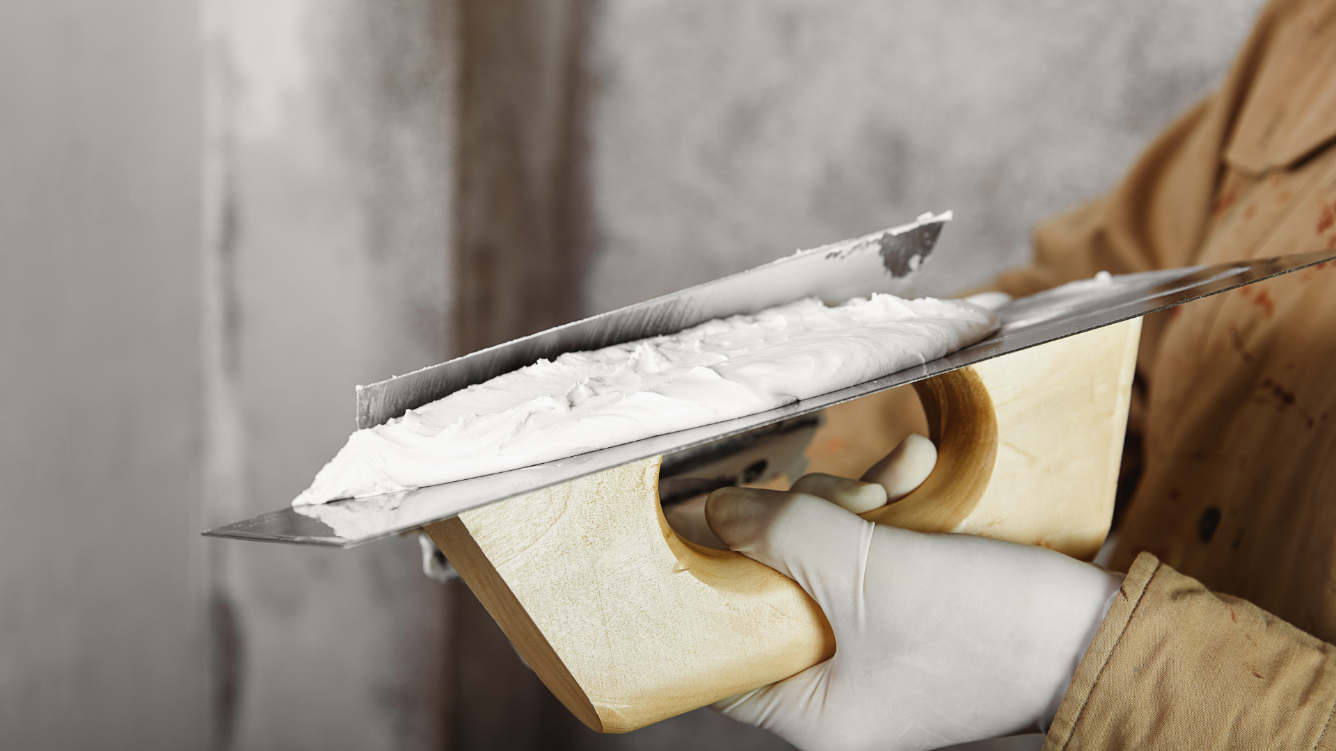 Person holding a trowel with white plaster, applying it to a wall.
