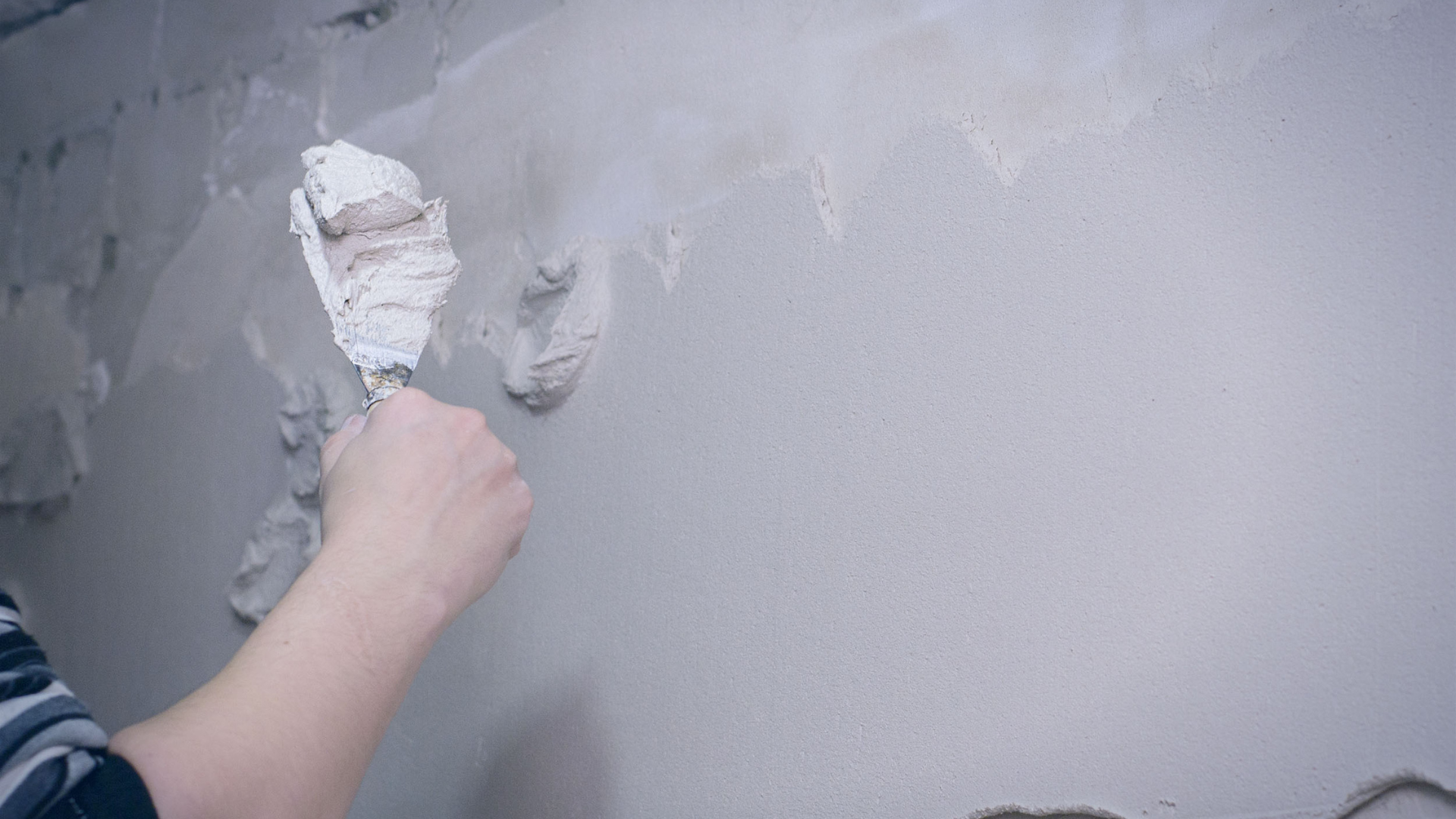 Person applying plaster to a wall with a trowel.