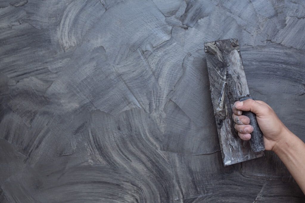 Hand with trowel smoothing textured gray wall finish.