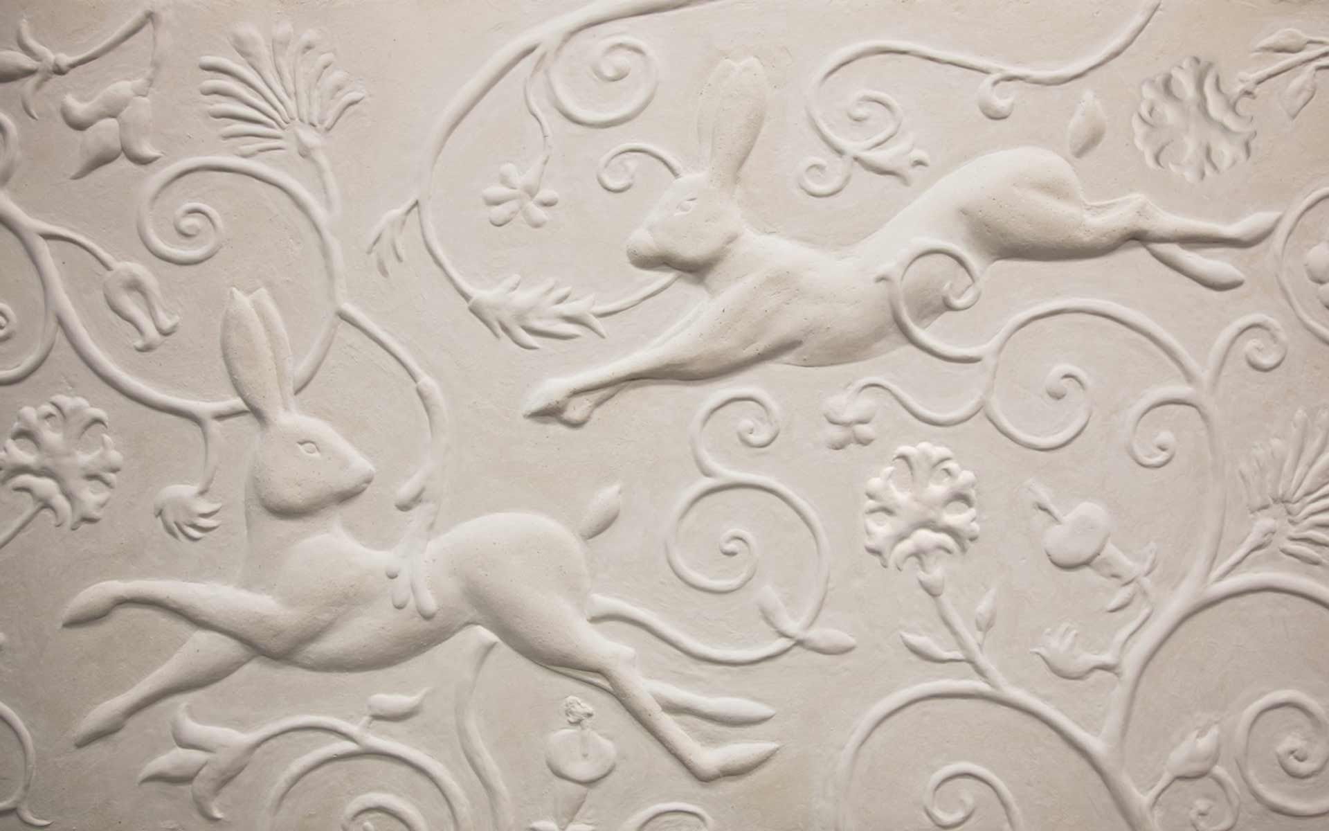 White plaster relief with two leaping hares among stylized floral vines.