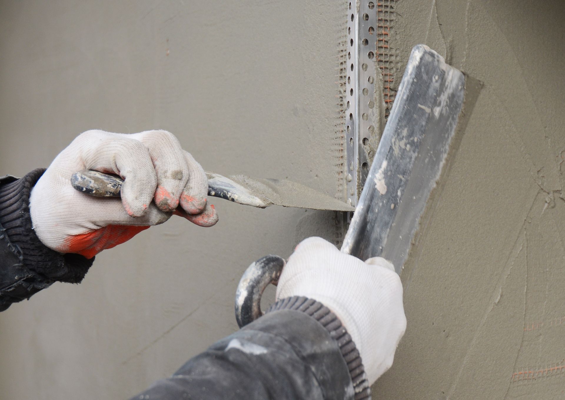Person applying plaster with a trowel, near metal corner bead, on a wall.