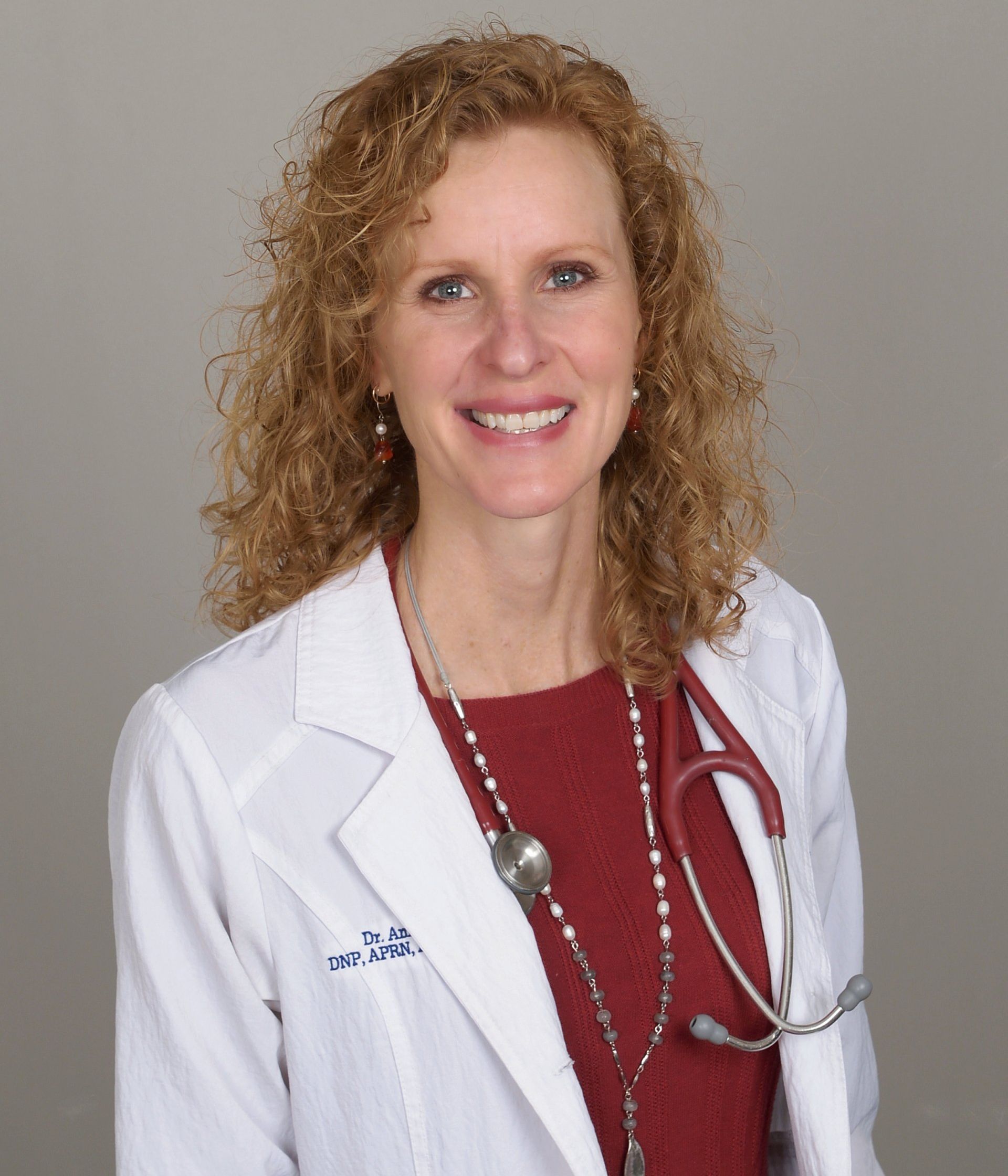 Woman with curly red hair, wearing a white coat and stethoscope.