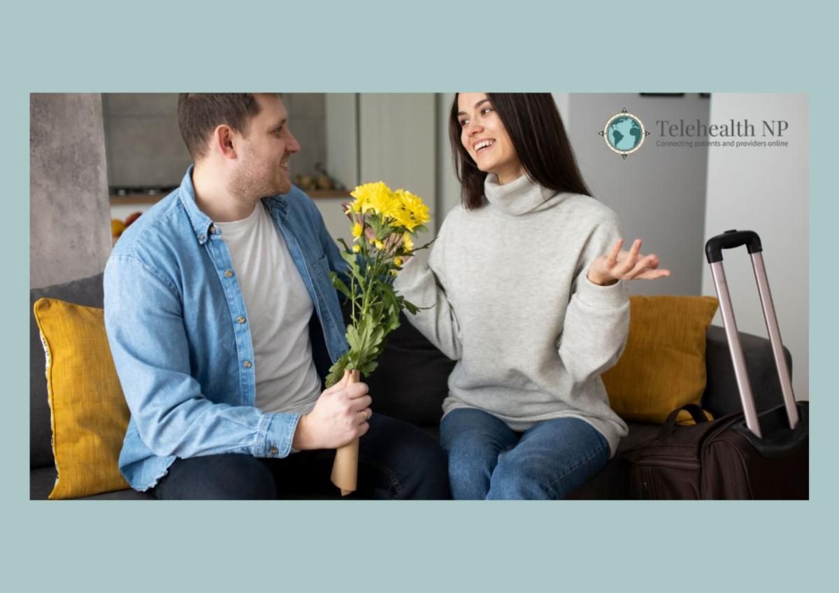 A man holds a yellow flower bouquet toward a woman sitting on a couch next to a suitcase.