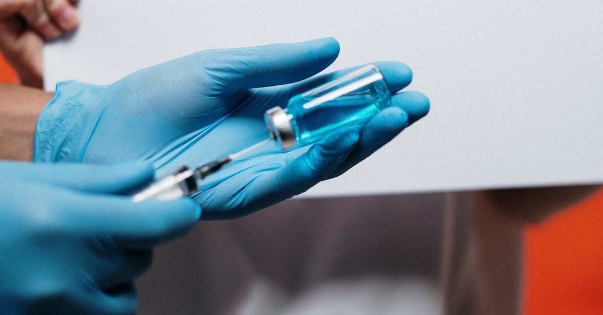 Gloved hands holding a vial of blue liquid and syringe, preparing an injection.