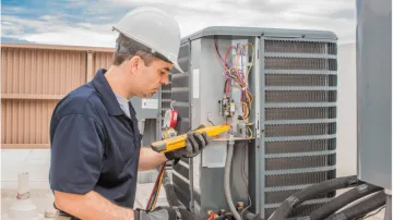 A man wearing a hard hat is working on an air conditioner.