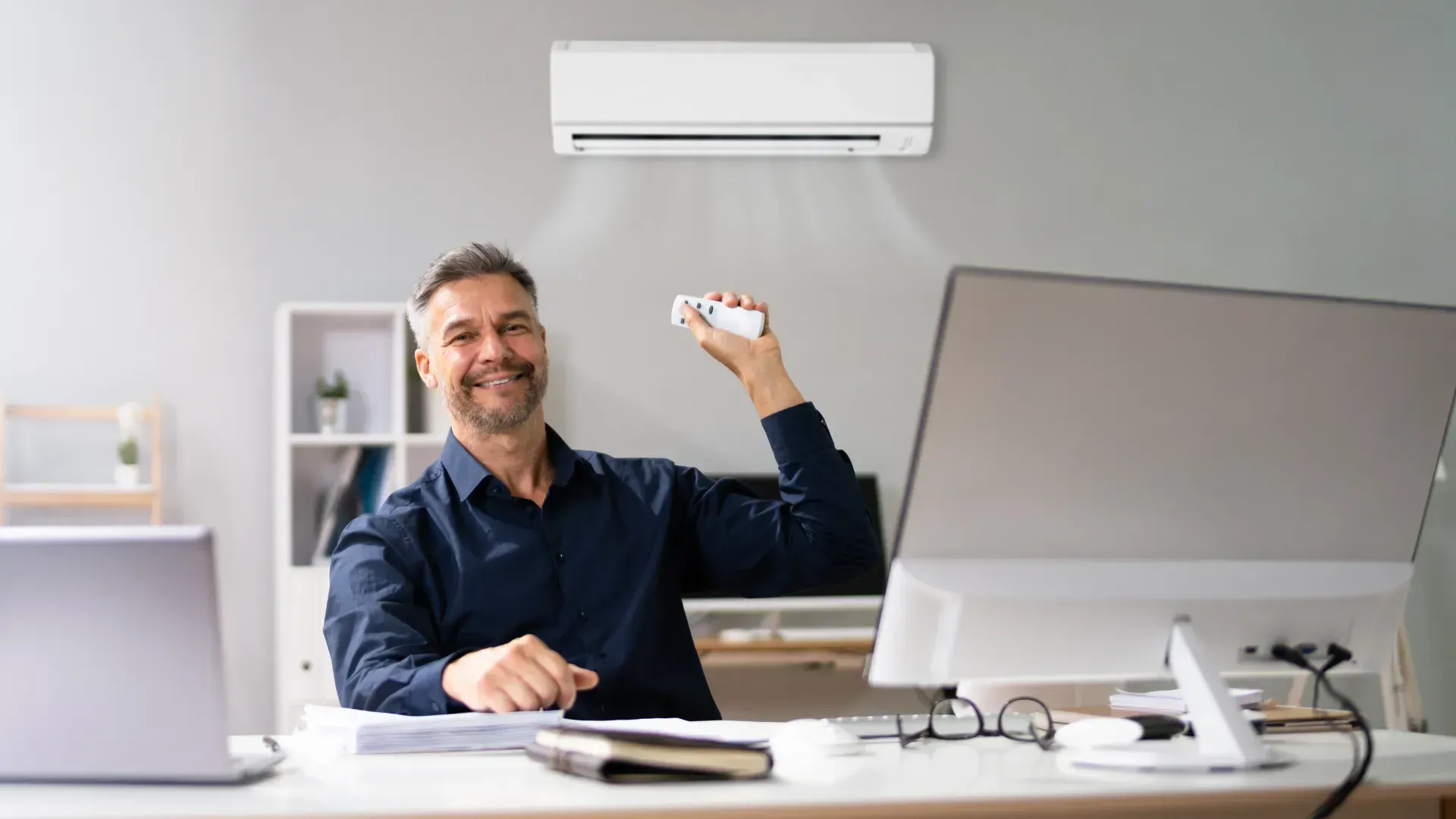 A man is sitting at a desk in an office holding a remote control.