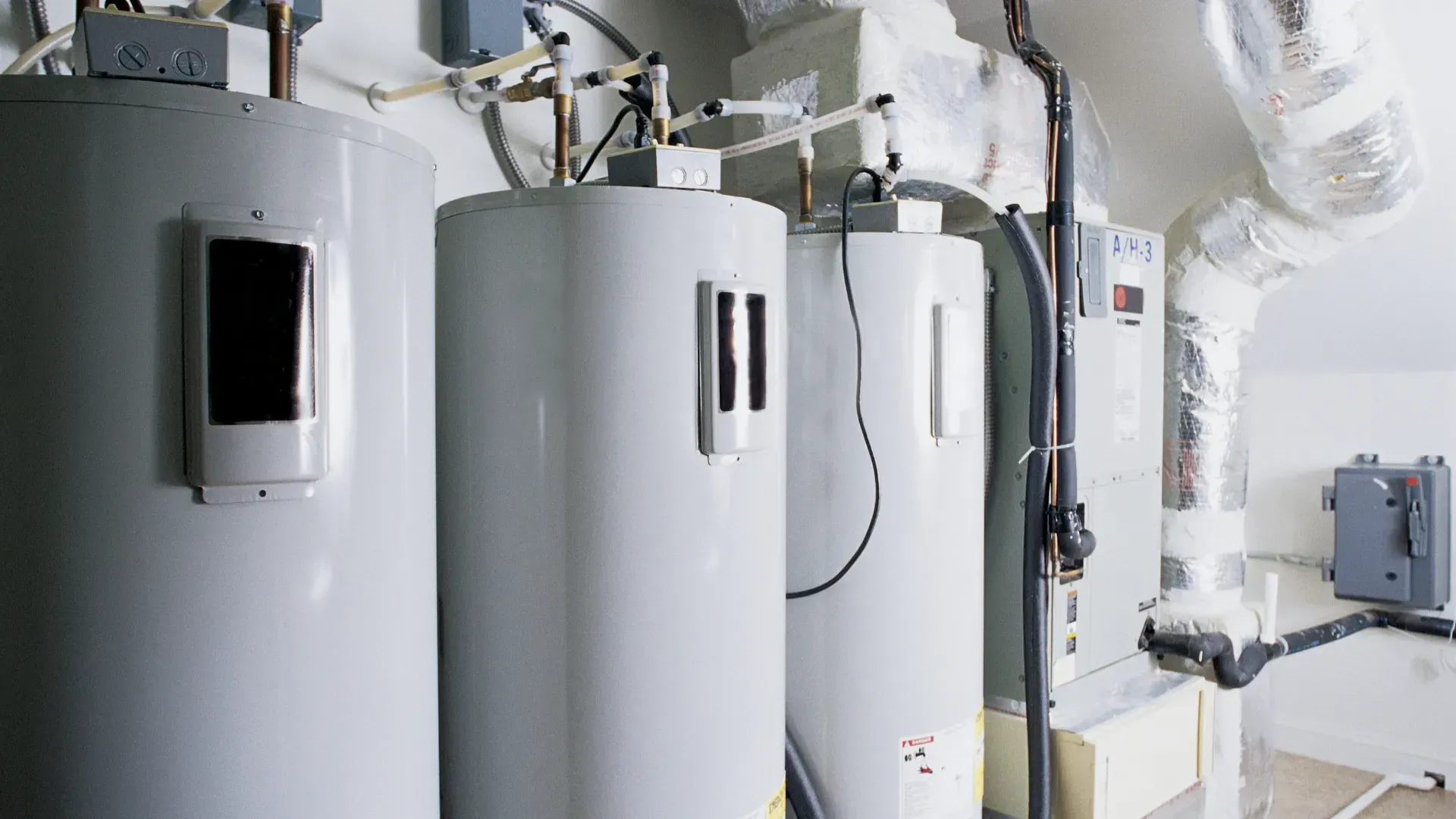 Three water heaters are sitting next to each other in a room.