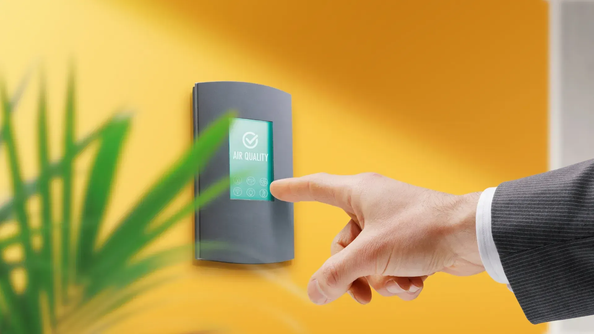A person is pressing a button on a wall next to a plant.