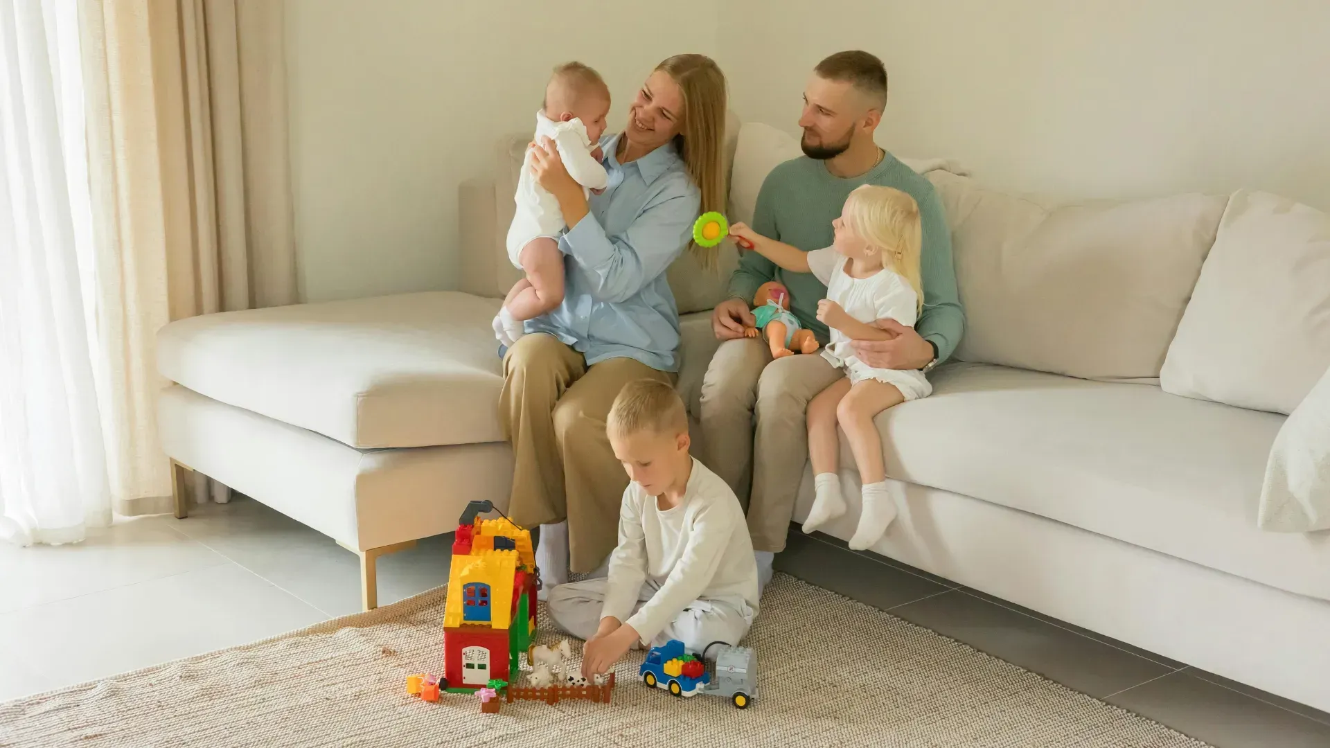 A family is sitting on a couch in a living room playing with toys.