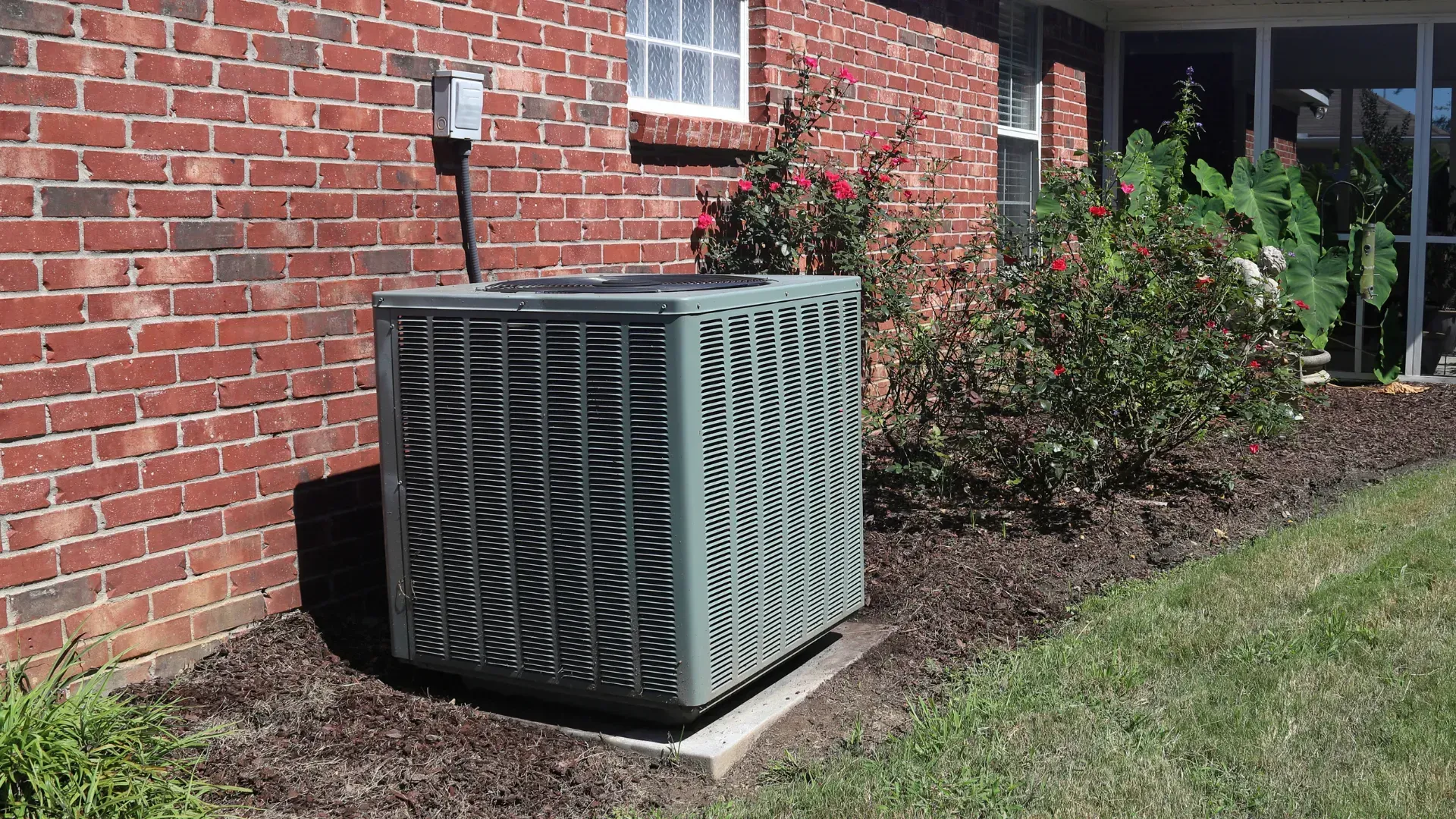 An air conditioner is sitting on the side of a brick house.