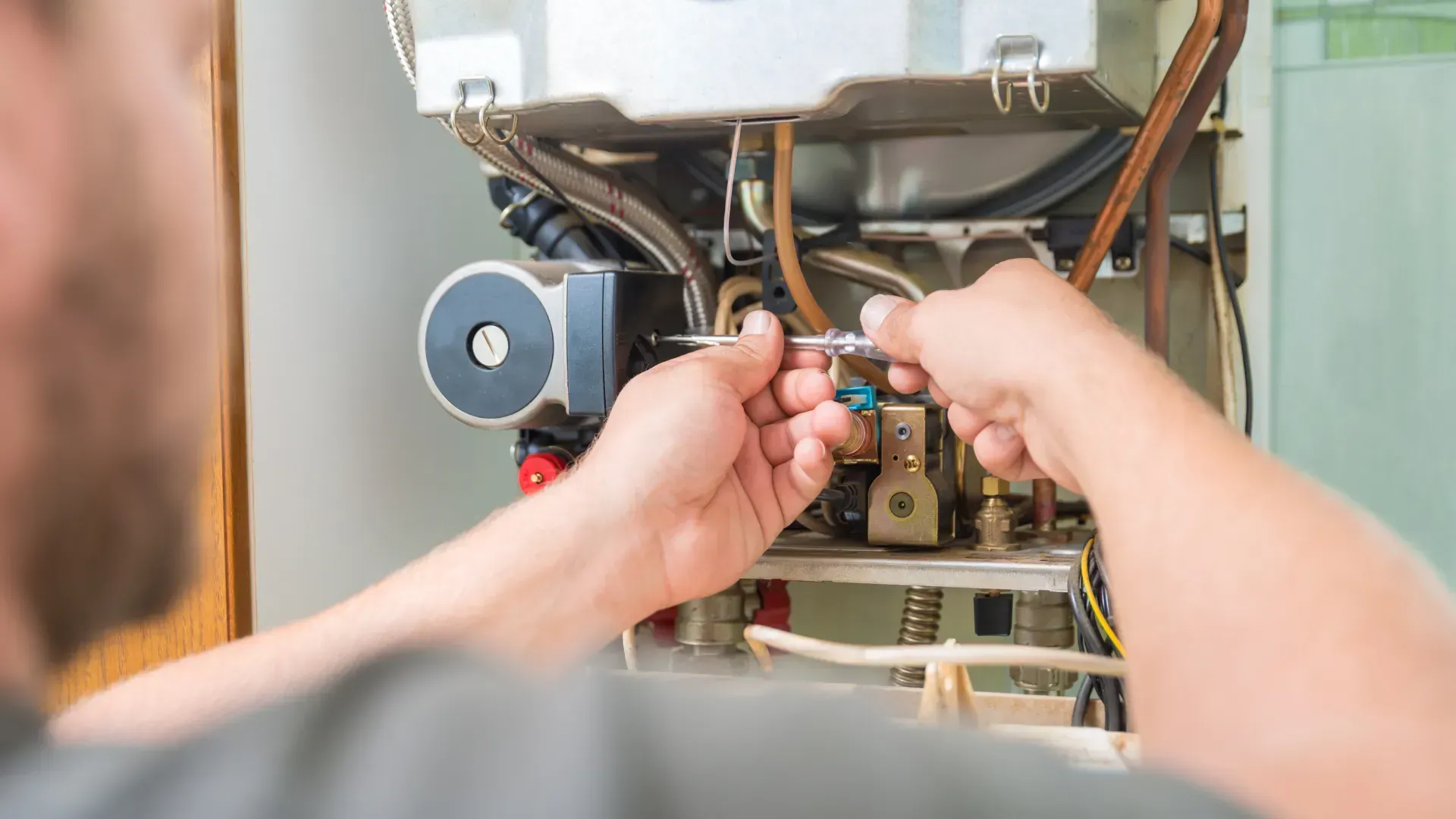 A man is fixing a boiler with a screwdriver.