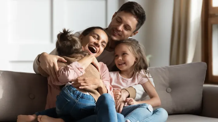 A family is sitting on a couch hugging each other.
