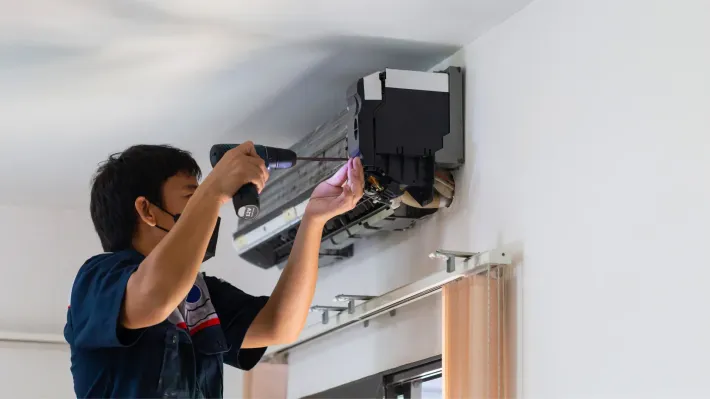 A man is fixing an air conditioner with a screwdriver.