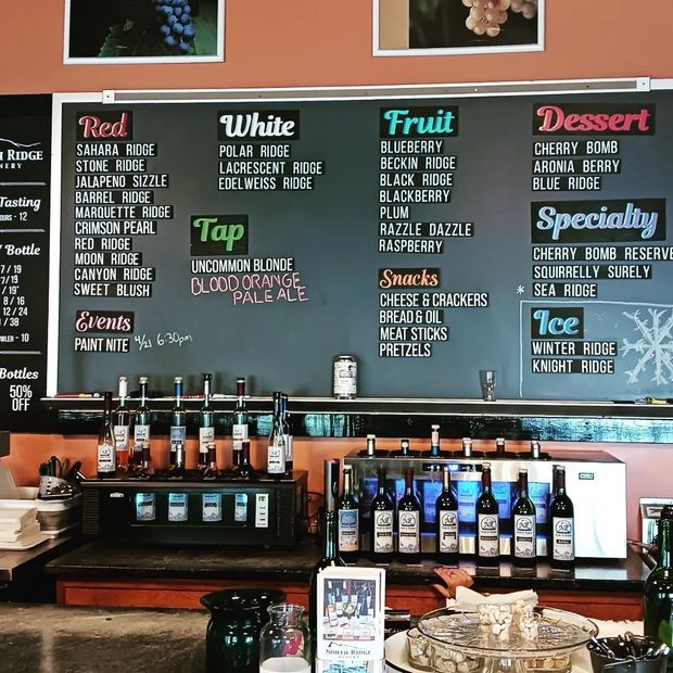 A menu board in a winery lists varieties of red, white, fruit, and dessert wines, plus specialty drinks, snacks, and events.