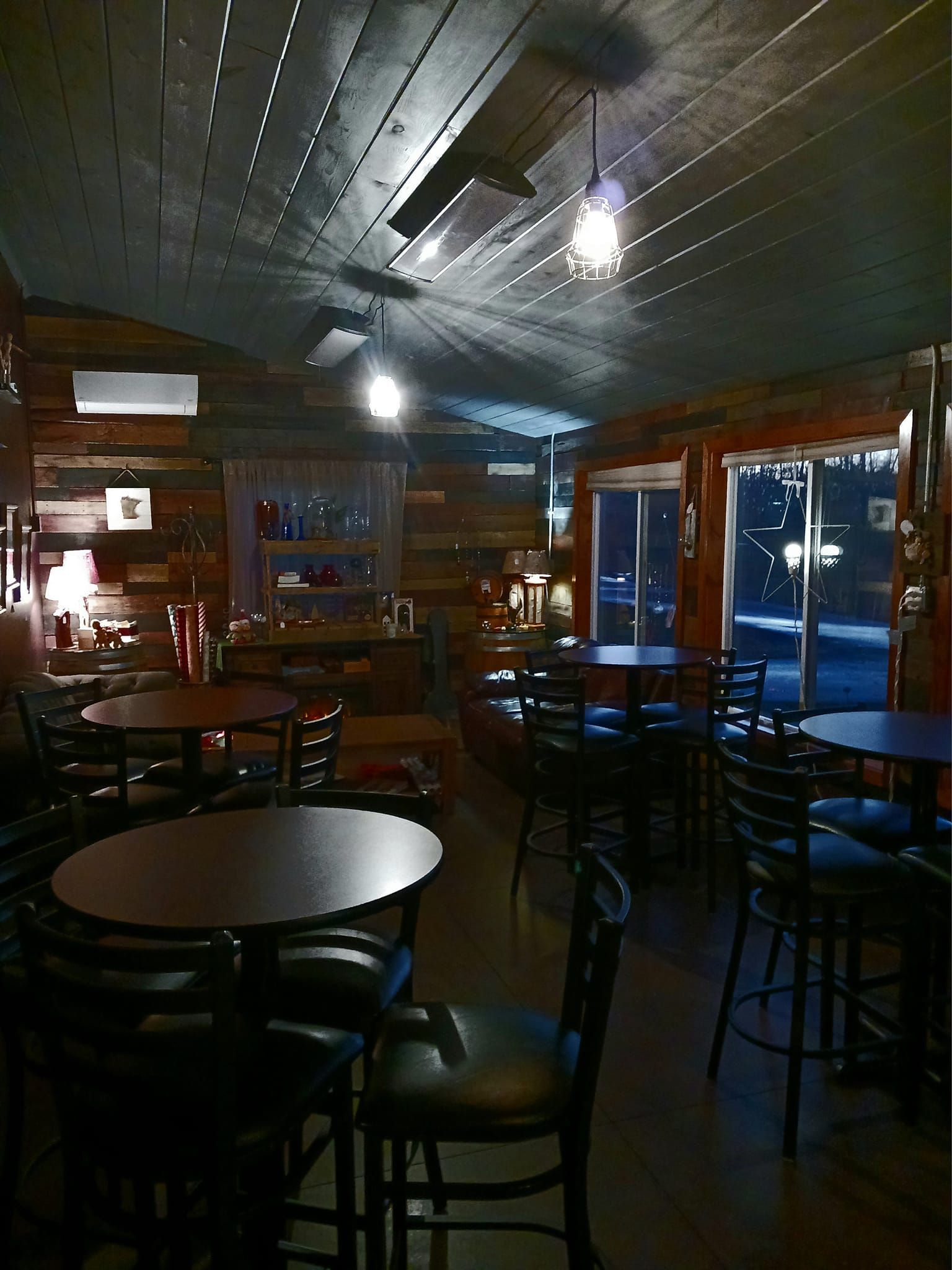 Dimly lit restaurant interior with dark wooden walls, multiple round tables, and black chairs.